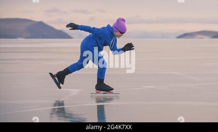 Das Kind trainiert auf Eisschnelllauf. Das Mädchen Schlittschuhe im Winter in Sportbekleidung, Sportbrille, Anzug. Zeitlupe im Freien. Stockfoto