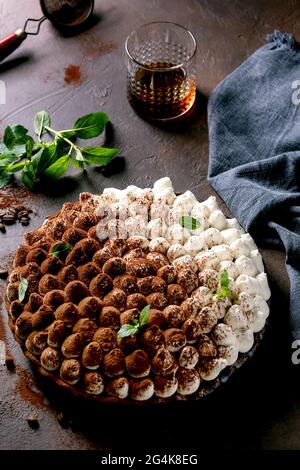 Hausgemachte glutenfreie Tiramisu traditionelle italienische Dessert mit Kakaopulver bestreut mit Minzblättern, Glas Whisky, blauen Textil-Napki dekoriert Stockfoto