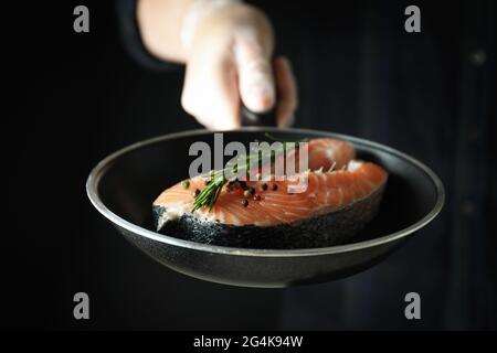 Männliche Hand in Handschuh Pfanne mit Lachsfleisch halten, Nahaufnahme Stockfoto