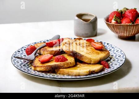 Vorrat an französischen Toasts mit frischen Erdbeeren auf Keramikplatte, Ahornsirup in Keramikkrug und Gabel über weißem Marmortisch. Speicherplatz kopieren Stockfoto