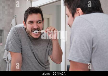 Junger latein, der sich morgens vor dem Spiegel im Bad die Zähne putzt. Umweltfreundliche Bambuszahnbürste. Stockfoto