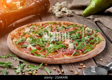 Pizza mit Prosciutto, Birne, Blauschimmelkäse, Pinienkernen und Rucola Stockfoto