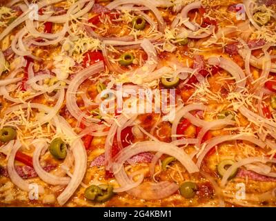 Eine Nahaufnahme der rohen Pizza vor dem Backen, mit Tomatensauce, Zwiebel, Käse, Salami, Oliven und roter Pfeffer Stockfoto