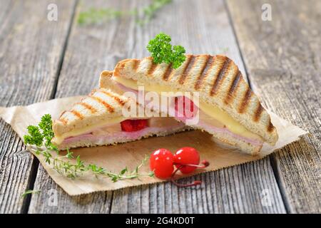 Gepresstes und geröstetes Sandwich im hawaiianischen Stil mit Schinken, Ananas und Käse auf Sandwichpapier auf einem Holztisch Stockfoto