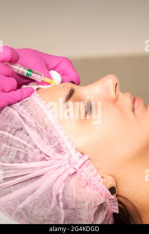 Die junge Frau erhält von einem Kosmetiker in einem Schönheitssalon eine Injektion mit Anti-Aging-Botox-Füllstoff auf die Stirn. Injektion der Gesichtsbehandlung Stockfoto