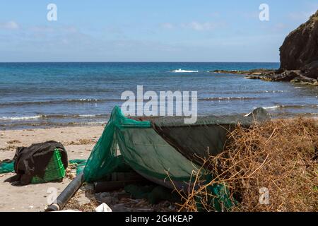 Fischernetz, das Boot bedeckt, das auf Strandsand gestrandet ist Stockfoto