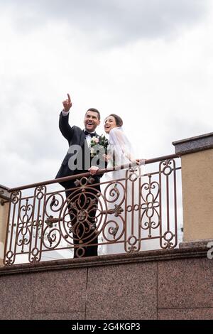 Blick aus der unteren Perspektive auf den lächelnden Bräutigam, der mit dem Finger in die Nähe der Braut auf der Brücke zeigt Stockfoto