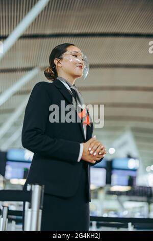 Flughafenbegleiter steht während einer Pandemie. Mitarbeiter der Fluggesellschaften mit Gesichtsschutz während einer Pandemie am Abflugsteig des Flughafens. Stockfoto