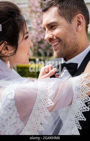 Seitenansicht der jungen Braut Anpassung Fliege auf lächelnde Bräutigam im Freien Stockfoto