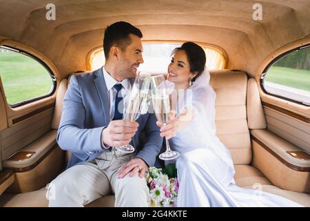 Lächelndes Brautpaar schaut sich an, während es mit Champagner im Auto toaste Stockfoto