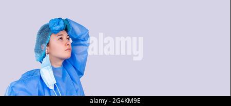 Banner, Langformat. Junge Ärztin ist es leid zu arbeiten. Grauer Hintergrund. Sie trägt blaue Uniform. Stockfoto
