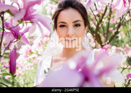 Brünette Braut Blick auf Kamera in der Nähe verschwommene Magnolienblumen Stockfoto