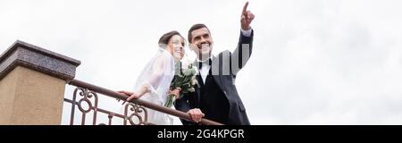 Niedrige Ansicht des Bräutigams, der mit dem Finger in die Nähe der Braut zeigt und im Freien Geländer, Banner Stockfoto