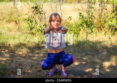 Defocus caucasian preteen Mädchen tun körperliche Bewegung im Park, Wald, im Freien, draußen. Gesunder Wellness-Lebensstil. Kniebeugen mit ausgestreckten Armen. Natur Stockfoto