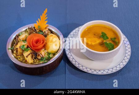 Biryani-Huhn mit Basmati-Reis und Suppe auf blauem Hintergrund. Traditionelle indische Küche. Stockfoto