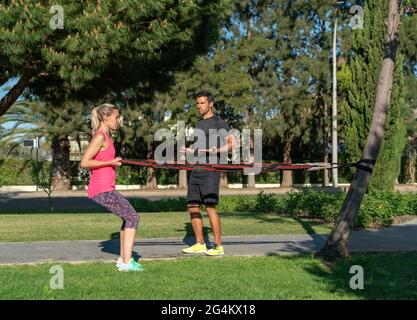 Fitnesstrainer und Client im Park üben Übungen mit einem Gummiexpander, Spannbänder. Im Freien im Park. Stockfoto