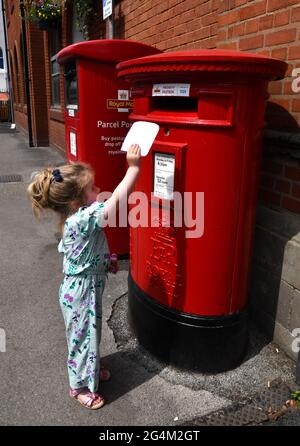 Kind, das einen Brief in einer traditionellen britischen roten Mailbox in England veröffentlicht. Säulenkasten Säulenkasten Briefkasten Briefkasten Briefkasten königliche Post Stockfoto