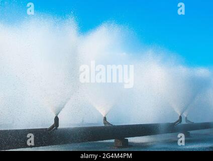 Brunnen aus einem System von Rohren, die Wasser in einem thermischen Kraftwerk kühlen. Spritzender Brunnen vor blauem Himmel im Industriegebiet. Stockfoto