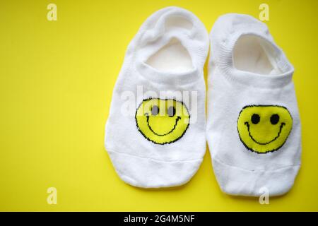 Zwei weiße Socken mit einem fröhlichen Smiley-Gesicht auf einem gelben Tisch. Stockfoto