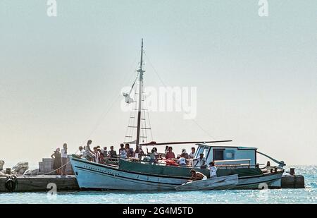 Gescanntes Bild eines Bootes, das im Hafen auf der kleinen Insel Pserimos vor Kos ankommt, der Einheimische, der sich anstellt, um seine Proviant circa 1984 A ph zu kaufen Stockfoto