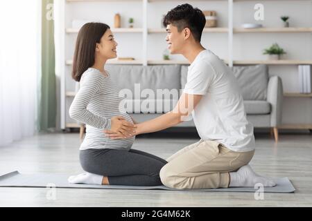 Junger asiatischer Mann hilft seiner Schwangeren Frau beim Trainieren Stockfoto