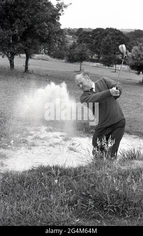 Siebziger Jahre, historisch, draußen auf einem Parkland-Golfplatz, ein Golfer mittleren Alters in einem Hemd und Krawatte, spritzt seinen Ball aus einem Bunker oder Sandfalle, England, Großbritannien. Stockfoto