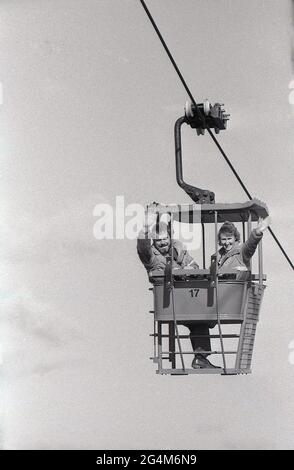 In den 1980er Jahren, ein Mann und eine Frau, die in einem neuen Ski- oder Sessellift auf einer künstlichen oder trockenen Skipiste im Freien fahren, Yorkshire, England, Großbritannien. Der zwei-Personen-Doppelstuhl war die beliebteste Art von Luftlift in der Ski-Industrie. In dieser Zeit wurden eine Reihe von trockenen Skipisten in Großbritannien gebaut, wobei die vielleicht bekannteste in Bracknell von John Nike im Jahr 1985 gegründet wurde. Es war eine der ersten und wenigen trockenen Pisten, die einen Sessellift hatten. Zu den berühmten Alumni gehören Eddie ‘The ‘Eagle’ Edwards. Stockfoto