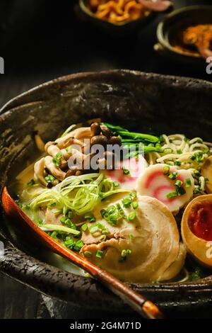 Ramen. Japanische gelbe Nudelsuppe mit Schweinebauch, Soja-Ei, Fischkuchen, Pilzen und grünem Gemüse. Stockfoto