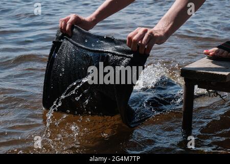 Junges Mädchen wäscht Kleidung von Hand in See. Handwäsche in der Natur. Wäsche waschen im See. Stockfoto