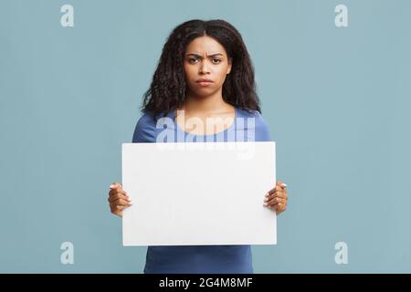 Öffentliches Demonstrationskonzept. Seriöse afroamerikanische Frau protestiert mit leerem Plakat, das auf blauem Hintergrund steht Stockfoto