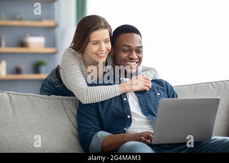 Portrait Of Loving Interracial Paar Mit Laptop-Computer Zusammen Zu Hause Stockfoto