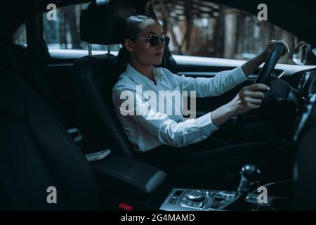 Schöne junge Frau Fahrer sitzt hinter dem Steuer in schwarzen modernen Auto. Blick auf den Innenraum des Fahrzeugs. Stockfoto