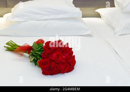 Strauß roter Rosen auf dem Bett in einem Hotelzimmer für die Flitterwochen. Romantisches Treffen der Gäste im Hotel. Stockfoto