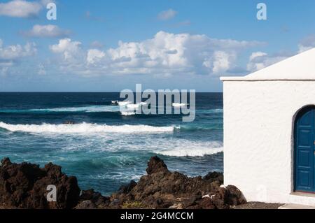 Kanarische Inseln, Lanzarote ,. Küstenlinie mit typisch schwarzen, gekühlten Lavagesteinen und starker Brandung. An der Küste befindet sich ein typisches weißes Haus. Stockfoto