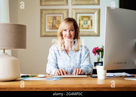Selbstbewusste Geschäftsfrau, die hinter ihrem Computer am Schreibtisch sitzt und arbeitet. Heimbüro. Stockfoto