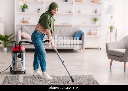 Unterer Abschnitt der Frau, die den Teppich mit einem Staubsauger reinigt Stockfoto