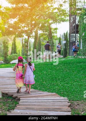 Rückansicht von asiatischen kleinen Mädchen im Kleid, die Seite an Seite auf dem Weg durch den grünen Garten gehen.zwei Freundinnen, die zusammen im Park gehen. Frohe Freunde Stockfoto