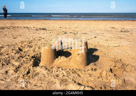 Eine verlassene Sandburg am Nordstrand von Mablethorpe in Lincolnshire mit einer Frau in der Ferne, die an einem heißen Sommertag entlang der Küste schaut. Stockfoto