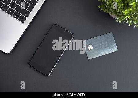 Laptop, Smartphone und elektronische Chipkarte auf mattgrauer Schreibtischoberfläche. Online bezahlen. Moderne Technik, drahtlose Geräte und Energieübertragung Stockfoto