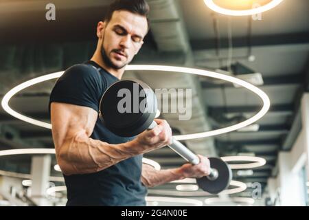 Hübscher junger sportlicher Bodybuilder, der Langhantel im Fitnessstudio macht Stockfoto