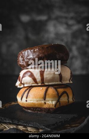 Stapel von drei verschiedenen frischen Donuts mit Schokolade und Karamell-Zuckerguss auf einem Holzbrett Stockfoto