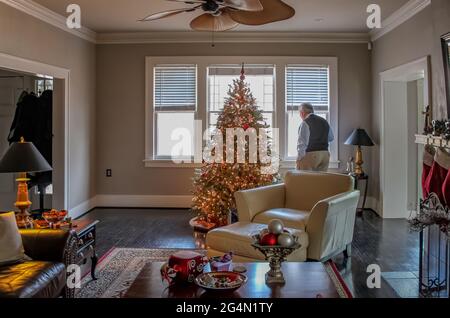 Im eleganten Haus, das zu Weihnachten mit einem Baum und Strümpfen geschmückt ist, blickt ein älterer Mann aus dem Fenster Stockfoto