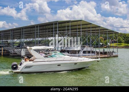 Luxus-Schnellboot mit rolltem Boot auf der Rückseite auf dem See im Sommer vorbei an überdachten Bootsanlegestelle mit schickeren Booten und No Wake Zone Schild Stockfoto