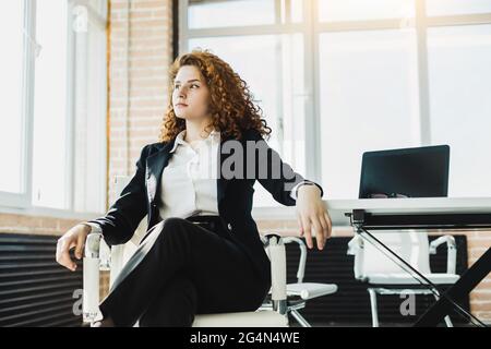 Porträt einer schönen jungen Geschäftsfrau mit roten lockigen Haaren, die produktiv im Büro arbeitet. Erfolgreiche Karriere und Mitarbeiter eines großen Unternehmens Stockfoto