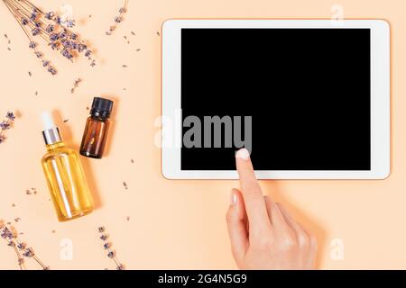 Draufsicht Frau Hand berühren Tablette mit leerem Bildschirm neben Bio-Hautpflegeprodukte auf beigem Hintergrund mit Lavendelblüten. Stockfoto