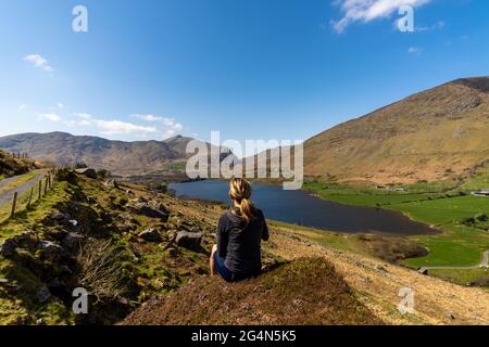 Eine sitzende Radfahrerin, die die Berglandschaft der Gap of Dunloe Kerry Mountains betrachtet Stockfoto