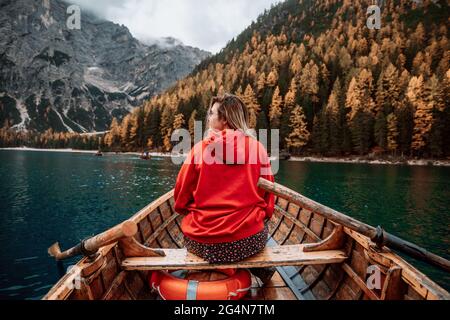 Rückansicht einer nicht erkennbaren blonden Frau auf einem Holzboot mit Paddeln, die auf dem türkisfarbenen Wasser des ruhigen Sees auf dem Hintergrund der majestätischen Landschaft von h schwimmen Stockfoto