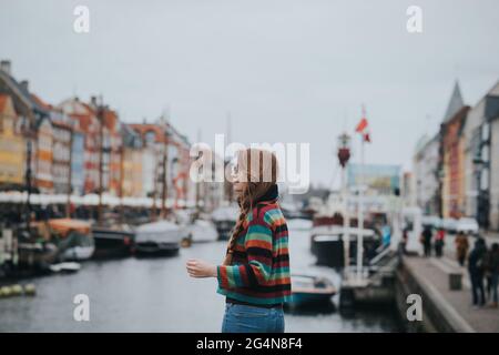 Seitenansicht einer Frau, die gegen Boote steht, die am Ufer des Kanals in Kopenhagen festgemacht sind Stockfoto