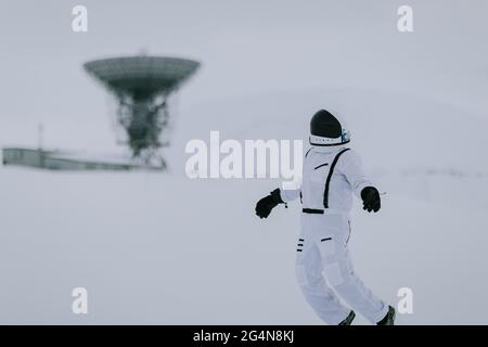 Nicht erkennbarer Kosmonaut im Raumanzügen, der im Winter im verschneiten Tal auf dem Hintergrund riesiger Radarantennen in Spitzbergen steht Stockfoto