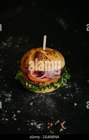 Leckerer veganer Burger mit frischem, reifen Gemüse, serviert auf schwarzem Hintergrund im Studio Stockfoto